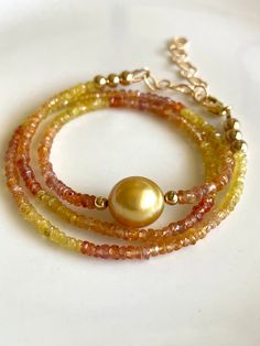 Petite sapphires, 2-4mm, ranging in color from yellow to peach, orange, and red, frame a gorgeous 10mm gold South Sea pearl.   The golden color is intense! Necklace measures 16" with 14K gold-filled findings, and comes with a 2" gold-filled extender chain to bring it to 18".  Works great as a versatile layering piece, or shines all on its own.   Your jewelry will come gift-boxed, and gift-wrapping is available upon request.  Thanks for checking out my shop! Gold Pearl Necklace With Rondelle Gemstone Beads, Gold Pearl Necklace With Gemstone Beads In Rondelle Shape, Gold Gemstone Beads For Jewelry Making, Gold Faceted Pearl Necklace Gift, Gold Briolette Gemstone Pearl Necklace, Gold Briolette Pearl Necklace With Gemstone, High Luster Yellow Gold Pearl Necklace With Round Beads, Gold Single Strand Gemstones As Gift, Elegant Gold Round Bead Gemstones