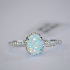 a white opal and diamond ring sitting on top of a table