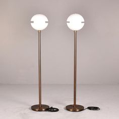 two floor lamps sitting next to each other on top of a white surface with one light turned off