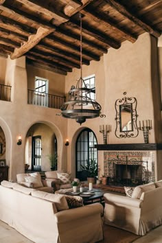 Rustic living room with high ceilings, wooden beams, a chandelier, beige sofas, and an ornate fireplace. Spanish Colonial Farmhouse, Spanish Art Deco Interior, Lime Paint Interior, Modern Spanish Style Homes Living Room, Spanish Style Hacienda Home, Traditional Colonial House Interior, Modern Spanish House Interior Design, Spanish Farmhouse Interior, Modern Heritage Home