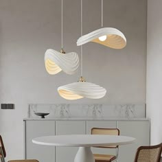 three lights hanging from the ceiling above a table with chairs and a vase on it