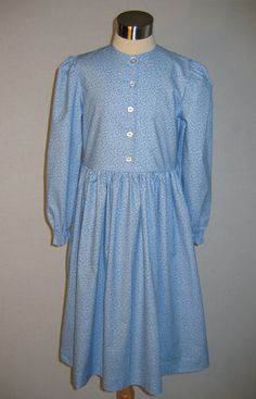 "Custom Girl's Prairie Dress A popular, simple dress for either a costume or everyday wear with a natural waist, gathered at the shoulder elbow length sleeves with narrow cuffs and a long, full skirt. This dress works well for everything from the late 1800's Little House look to the early 1900's. For winter, it is also available with long sleeves that end with slip over cuffs. The bodice buttons down the front and the full skirt is gathered at the waist. If you would like a longer than standard Classic Dress With Smocked Cuffs, Cotton Prairie Dress For Daywear, Classic Fitted Dress With Smocked Cuffs, Classic Fitted Long Sleeve Prairie Dress, Fitted Long Sleeve Prairie Dress With Buttons, Cotton Long Sleeve Prairie Dress, Fitted Peasant Dress With Puff Sleeves For Daywear, Fitted Long Sleeve Prairie Dress With Gathered Sleeves, Classic Cotton Prairie Dress For Daywear