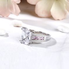 Luxurious and breathtaking, this engagement ring honors the light of your life.Crafted in sterling silver, the ring features a large radiant-cut center stone and three row paved of stones on the shank. They show a sparkling look from every angle. The channel-set pink stones in the middle of the shank adds elegance to it. Treat yourself or surprise her with this masterpiece!Carat Weight: 9.3 ctStone Size: 10*12 mmStone Type: Jeulia® StoneNumber of Stones: 1 Stone Color: Diamond WhiteStone Shape: RadiantCarat Weight: 0.88 ctStone Size: 1,1.2,2.5,2.5,1.1 mmStone Type: Jeulia® StoneNumber of Stones: 58 Stone Color: Diamond White, Fancy PinkStone Shape: RoundWeight: 7.82 gWidth: 12.56 mmHeight: 7.95 mmThickness: 3.92 mmMaterial: 925 SilverPlating Color: Silver Fine Jewelry With Cubic Zirconia And Side Stones, Fine Jewelry In Diamond White With Side Stones, Diamond White Jewelry With Side Stones As Gift, Fine White Jewelry With Side Stones, White Radiant Cut Cubic Zirconia Diamond Ring, White Cubic Zirconia Diamond Ring In Radiant Cut, White Cubic Zirconia Diamond Ring Radiant Cut, White Cubic Zirconia Radiant Cut Ring, Princess Cut Jewelry With Side Stones As Gift