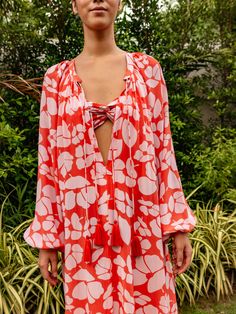 Embrace the thrill of summer and elevate your style with our Calista silk caftan. Crafted from luxurious silk crepe, it flaunts delicate tassels and a vibrant persimmon poppy print. The neckline is adorned with double tassels, exuding an extra touch of grace. Step into strappy sandals for a bold and chic look. The Calista Silk Caftan is the ultimate choice for warm weather, whether you're soaking up the sun at the beach or lounging by the pool. With its airy and effortless fit, it's perfect for throwing over a bathing suit or lounging in daring fashion! Color : Persimmon Poppy 100% Silk Crepe Relaxed Fit Tassels Spring Beach Viscose Tunic, Beach Viscose Tunic, Spring Beach Tunic Made Of Viscose, Summer Beach Tunic In Viscose, Summer Flowy Silk Crepe Dress, Silk V-neck Tunic For Summer, Long Sleeve Silk Beach Dress, Spring Viscose Long Sleeve Kaftan, Elegant Viscose Tunic For Summer