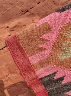 a pink and brown rug sitting on top of a wooden floor next to a brick wall