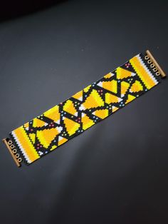 a yellow and black beaded wristband with geometric designs on the end, sitting on top of a table