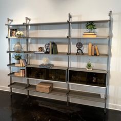 a book shelf with books and plants on it in a room that has black floors