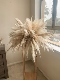 a tall white plant sitting on top of a wooden stand in front of a window