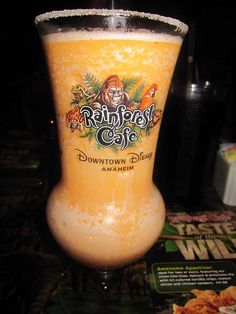 a tall glass filled with orange liquid sitting on top of a table next to a menu