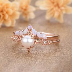 a close up of a ring on a table with flowers in the background and a white pearl