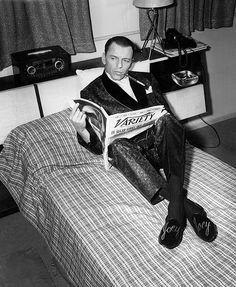 a man sitting on top of a bed reading a newspaper