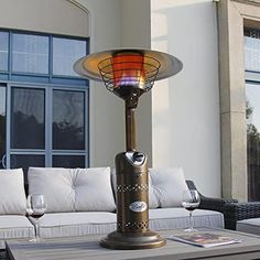 an outdoor table with wine glasses on it and a lamp in front of the window