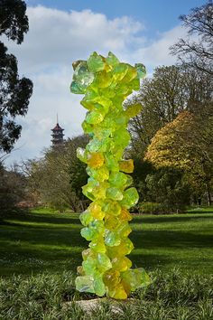 a tall yellow glass sculpture in the middle of a grassy area with trees and buildings in the background