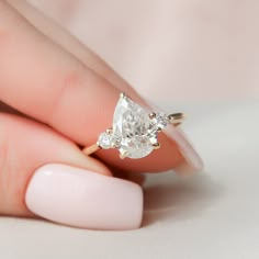 a woman's hand holding an engagement ring with a pear shaped diamond