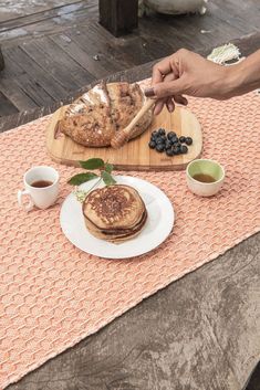 a person is cutting up some food on a wooden table with cups and saucers