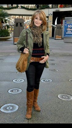 a woman is standing on the sidewalk with her hand in her pocket and wearing boots