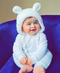 a baby sitting in a blue chair wearing a white bear hat