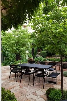 an outdoor dining table surrounded by trees and plants in a courtyard area with stone pavers flooring