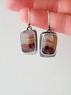 A pair of rounded rectangular Laguna Lace agate pairs are set in fine and sterling silver. Colorful bands of deep red, periwinkle and rose move in wavy stripes through the stones: a beautiful desert sunset palette. A free-moving back layer of sterling silver mirrors the shape of the stone and extends down below it to show the unique texture of silver dust fused to silver. A window cut behind the stones allows you to view the backside of these unusual natural agates. The silver is oxidized to give a beautiful contrast between the stones and the textured metal. These one of a kind earrings measure 1 5/8" in length from the top of the ear wire, and 1/2" wide. Artisan Nickel-free Rectangular Earrings, Agate Gemstone Earrings Gift, Agate Gemstone Earrings For Gifts, Unique Nickel Free Rectangular Jewelry, Unique Nickel-free Rectangular Jewelry, Silver Rectangular Jewelry With Natural Stones, Modern Earrings With Rectangular Stone Gift, Rectangular Silver Jewelry With Natural Stones, Modern Rectangular Stone Earrings For Gifting