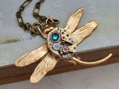 Vintage 17 jeweled watch movement mounted on top of brass Victorian style dragonfly and accented with blue zircon rhinestone on top. Pendant hangs on 16 antiqued brass chain with lobster clasp. All metal parts torch soldered together. Please allow minor differences for each watch movement than sample pictures shown. Measurement, Pendant is about 1.9 inch (48mm) wide on 16 inch chain. If you have a preferred length for the chain, please let me know in message to seller box and I will adjust it be Steampunk Antique Gold Jewelry Gift, Antique Gold Steampunk Jewelry Gift, Antique Gold Steampunk Jewelry As Gift, Antique Gold Steampunk Jewelry For Gift, Steampunk Gold Necklace With Vintage Charm, Steampunk Gold Jewelry With Antique Finish, Steampunk Gold Brass Necklace, Gold Steampunk Nickel-free Jewelry, Gold Steampunk Brass Necklace