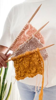 a woman holding knitting needles in front of her stomach with yarn on it and another crocheted item behind her