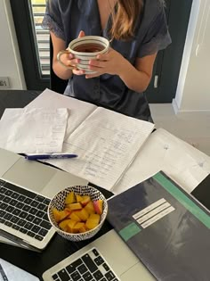 a woman sitting at a desk holding a bowl of fruit in front of her laptop