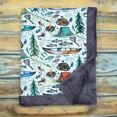 a blanket with an image of boats and trees on it, sitting on a wooden surface