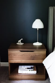 a night stand with a lamp on it next to a bed