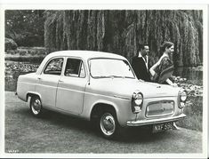 an old photo of a man and woman standing next to a car in the grass