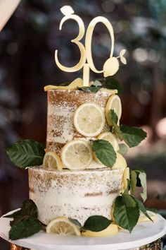 a wedding cake with lemons and leaves on the top is decorated with gold numbers