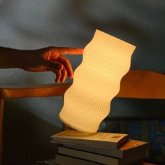 a person is pointing at a lamp on top of books in front of a chair