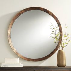 a mirror sitting on top of a wooden dresser next to a vase with a plant in it