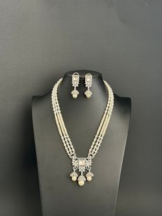 Embrace the timeless elegance and dazzling charm of our White Pearl Kundan CZ Long Necklace, a masterpiece designed to captivate and enchant. Handcrafted with meticulous attention to detail, this exquisite piece is not just a necklace, but a statement of sophistication that transcends the ordinary. Kundan Classic Mala Necklace With Black 2 Tone Rhodium Plating Pendant Height = 60 mm || Width = 50 mm Earring Height = 45 mm || Width = 16 mm Length = 16 Inch Kundan Necklace Set with chain closure   This is 100% Handmade jewelry. So the color, shades, and texture displayed may vary slightly from the actual product due to digital image limitations. We request you consider these minor variations. Please expect the possibility of some slight imperfections when buying handmade jewelry. If you have Luxury Dual-tone Silver Temple Necklace, Elegant Kundan Bridal Sets For Eid, Silver Jewelry Sets With Stone Work For Eid, Silver Jewelry Sets For Eid, Silver Hand Set Jewelry For Eid, Eid Silver Jewelry Sets With Stone Work, Elegant Meenakari Bridal Sets For Eid, Elegant Bridal Sets For Eid Festivities, Elegant Bridal Sets For Eid