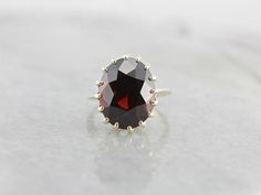 This ring features a simple and classically designed mounting, sized perfectly for a cocktail piece! The structural pattern of the shoulders lends a sense of light and grace to the mounting. Shaped in a perfect oval, the deep red of the garnet in the center adds a lovely pop of color to a simple but classic ring! Metal: 14K Yellow Gold Gem: Garnet 13.82 Carats Gem Measurements: 11.9 x 15 mm, Oval Ring Size: 5 Elegant Oval Ruby Ring For Gift, Elegant Oval Ruby Ring With Center Stone, Elegant Oval Ruby Ring For Anniversary, Elegant Yellow Gold Ruby Ring For Formal Occasions, Heirloom Oval Rings For Formal Occasions, Formal Heirloom Oval Rings, Elegant Gold Ruby Ring With Oval Cabochon, Timeless Ruby Ring With Prong Setting For Formal Occasions, Timeless Ruby Ring With Prong Setting For Formal Events