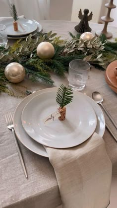 the table is set for christmas dinner with silverware and greenery, including pine cones