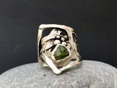 "A ring that takes us to ancient times, made of sterling silver and raw Peridot. Its abstract, unusual and at the same time organic shape contain a vibrant raw peridot in its center which gives even more strength to the composition. The ring has been aged with an oxidation patina and then cleaned, and this makes its texture visible even more. Wide at the front and narrow at the back, it is comfortable and beautiful to wear. This piece is entirely made by myself, soldering sterling silver (925) with traditional Jewelry techniques. Every piece is unique! Size ring:  adjustable from  US size : 7 1/2 to 8(please write me your size, I'll set it) Peridot: 0,31\" x 0,35\" 8 x 9 mm Band width: 0,27\" 7 mm Top ring size: 1,02\" 26 mm Don't know your ring size? Go here: http://www.onlineconversion.c Unique Raw Sterling Silver Ring, Unique Sterling Silver Ring With Raw Details, Organic Jewelry Design, Statement Rings Unique, Rough Jewelry, Bezel Set Engagement Ring, Antler Jewelry, Raw Stone Ring, Unusual Rings