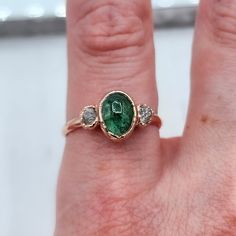 a close up of a person's hand wearing a ring with a green stone