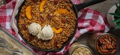 a skillet filled with granola, ice cream and sliced peaches on top of a checkered table cloth