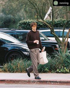 a man walking down the street with a bag and coffee in his hand while wearing sunglasses