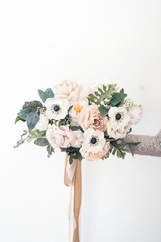 a bridal bouquet with white flowers and greenery is held by a woman's arm