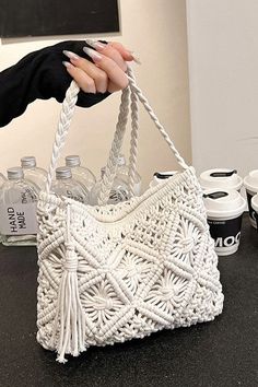 a woman holding a white purse on top of a counter next to cups and bottles