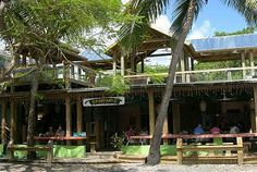 people are sitting at tables in front of a building with green walls and palm trees