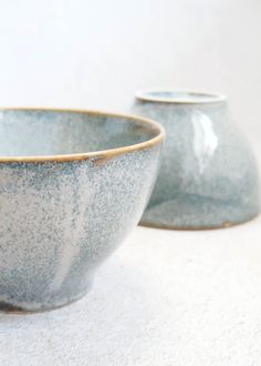 two blue bowls sitting next to each other on a white counter top, with one empty bowl in the foreground