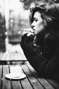 black and white photograph of a woman sitting at a table with a cup of coffee