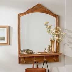 a mirror, purse and flowers on a shelf in front of a wall mounted mirror