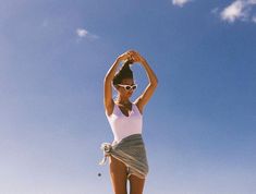 a woman standing on top of a sandy beach next to a surfboard under a blue sky