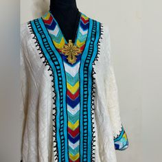 Ethiopian And Eritrean Traditional Dress, Habesh Kemis, Beautiful,Simple,Featuring Intricate Embroidery With Vibrant Colors. The Design Suggests It Might Be From A Specific Cultural Or Ethnic Background. The Dress Has A Prominent V-Shaped Neckline With Multicolored Geometric 100%Cotton White V-neck Festive Kurta, Blue Traditional Kurta With Embroidered Neckline, Traditional Blue Kurta With Embroidered Neckline, Festive White Kurta With Embroidered Neckline, White V-neck Kaftan For Festive Occasions, White Long Sleeve Kurta With Embroidered Neckline, White V-neck Embellished Kaftan, White Bohemian Tunic With Resham Embroidery, Traditional White Embellished Kaftan