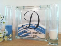 a glass block with the letter d on it next to a candle and some flowers