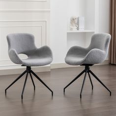 two gray chairs sitting on top of a hard wood floor next to a white wall