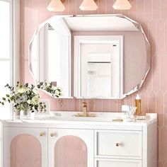 a bathroom with pink wallpaper and white vanity, round mirror on the wall above it